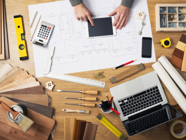 Construction engineer and architect's desk with house projects, laptop, tools and wood swatches top view, male hands using a digital tablet